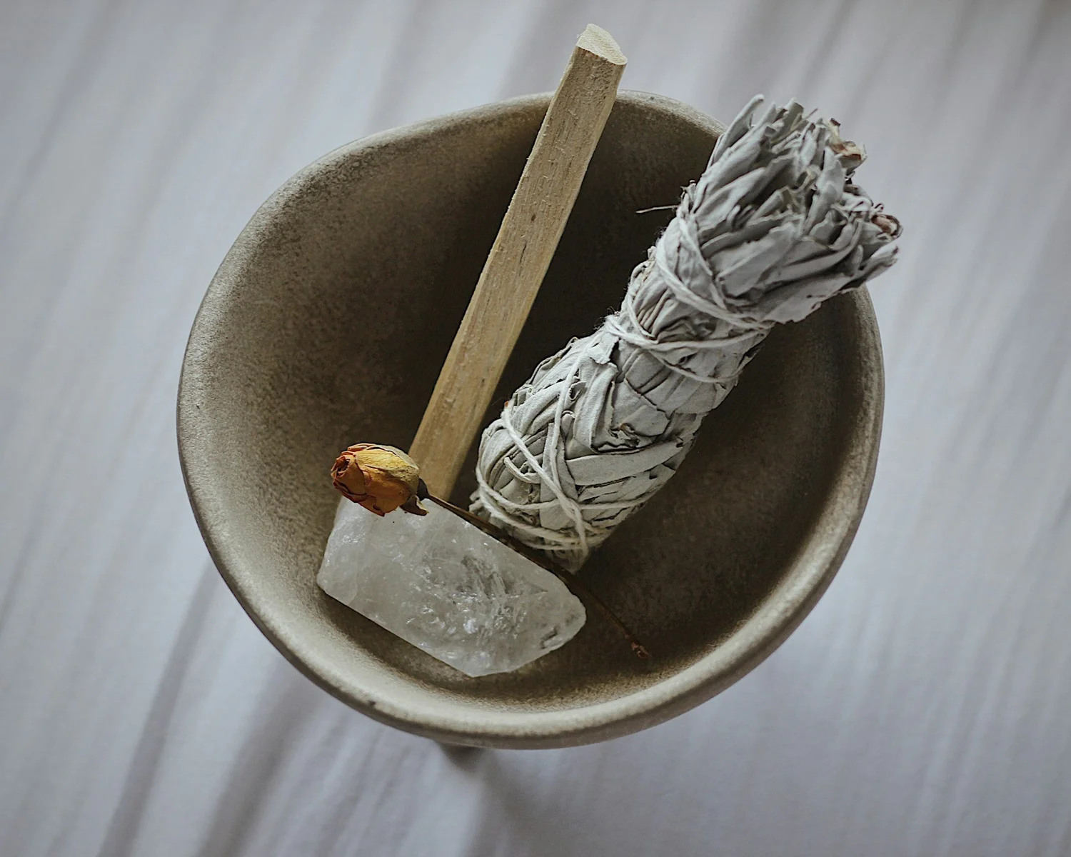 A bundle of dried sage and a small crystal resting in a stone bowl